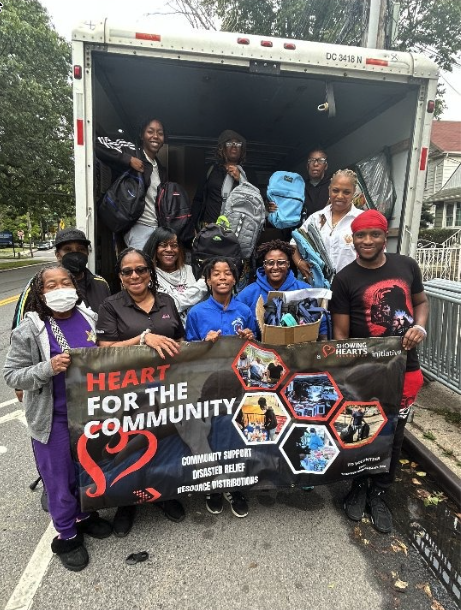 Volunteers loading backpacks and supplies into a truck behind a Heart for the Community banner